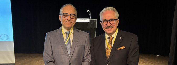 Chief Judge Rowan Wilson and another man in suits and glasses stand side by side on a stage in front of a podium with a microphone, discussing recent funding increases for Family Court Reform.